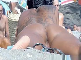 Tattooed nude woman sunbathing at nudist beach