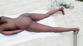 Ebony girl masturbates in the sand while being filmed