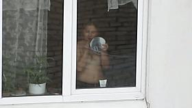 A hot topless chick puts on her makeup by a window