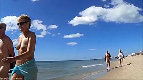 Group of mature nudists walks around the beach naked