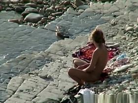 Nudist woman with sunglasses at the rocky beach