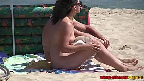 Naked woman is enjoying on the beach while people are staring at her trimmed pussy